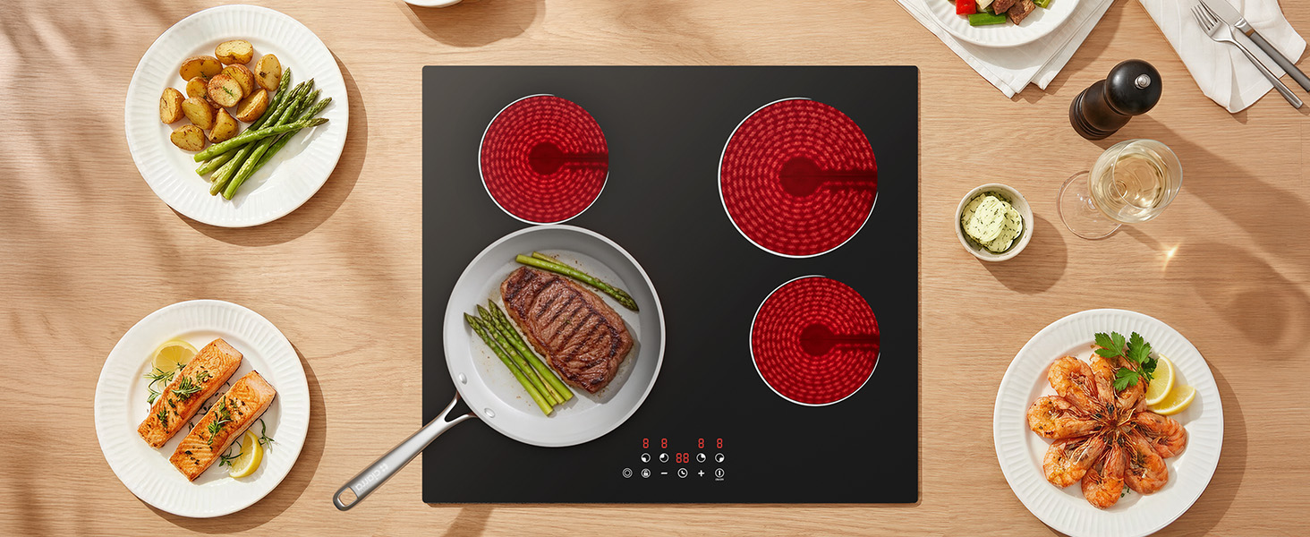Overhead view of black glass cooktop with red circular burner indicators. Multiple plates of prepared food with asparagus and meat visible around the cooking surface.