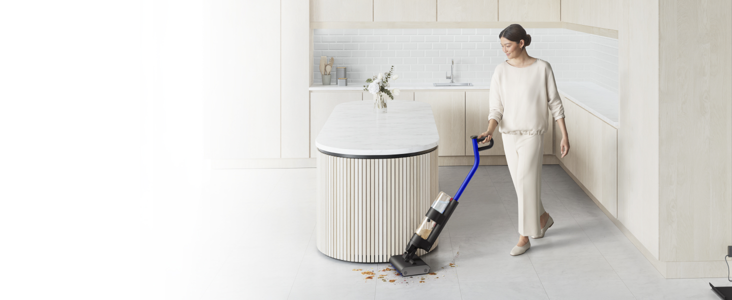 A woman cleaning up a wet spill on the kitchen floor with the Dyson WashG1 wet floor cleaner.
