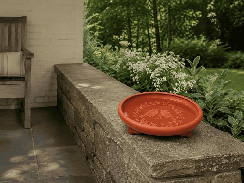 Red terracotta bird bath resting on a broad stone garden wall beside a covered veranda.