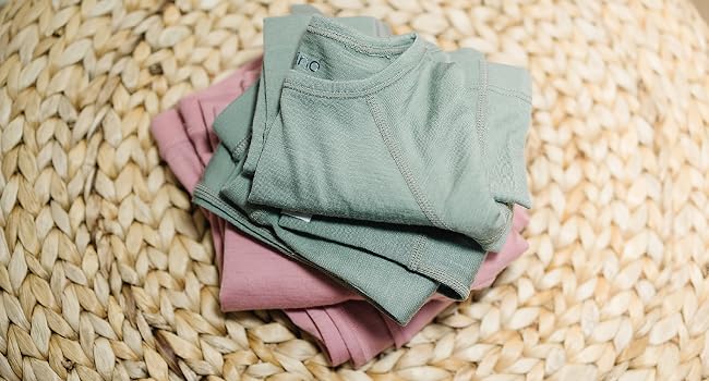 Folded pile of Woolino Kids' Merino Wool Thermal Tops & Leggings in Sage green and Blush pink.